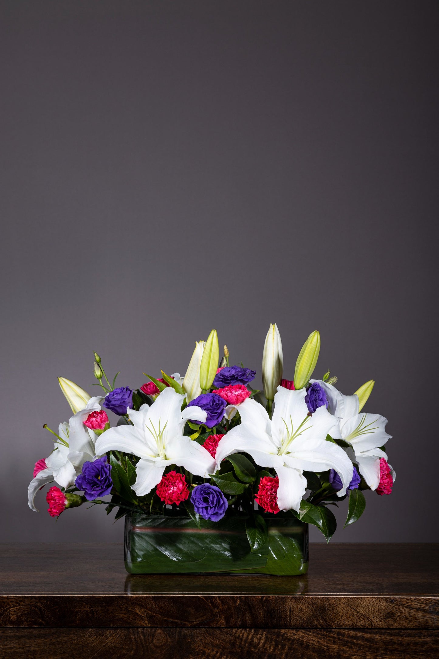 Casa Blanca - Elegant centerpiece with pure White Lilies and colorful Spray Carnations in a lush foliage bed | Flower delivery in Bengaluru | Buy flower bouquets online Bengaluru | Same-day flower delivery Bengaluru | Online florist Bengaluru | Order flowers online Bengaluru | Luxury flower bouquet in Bengaluru