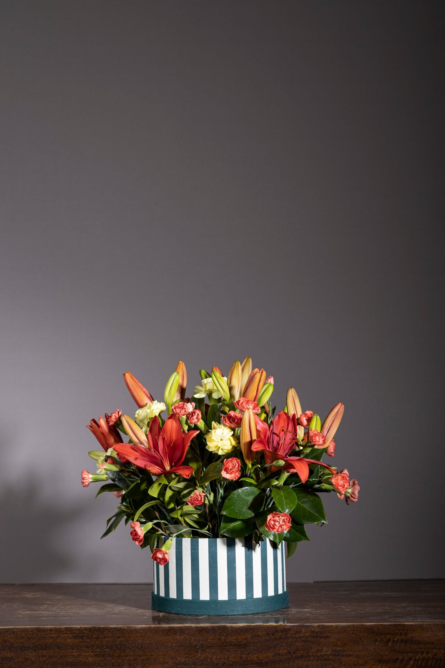 Twilight – A stunning custom keepsake hat box featuring a delightful mix of orange lilies, red carnations, and green chrysanthemum blossoms. A perfect floral gift for birthdays, anniversaries, thank you gestures, congratulations, and new baby celebrations