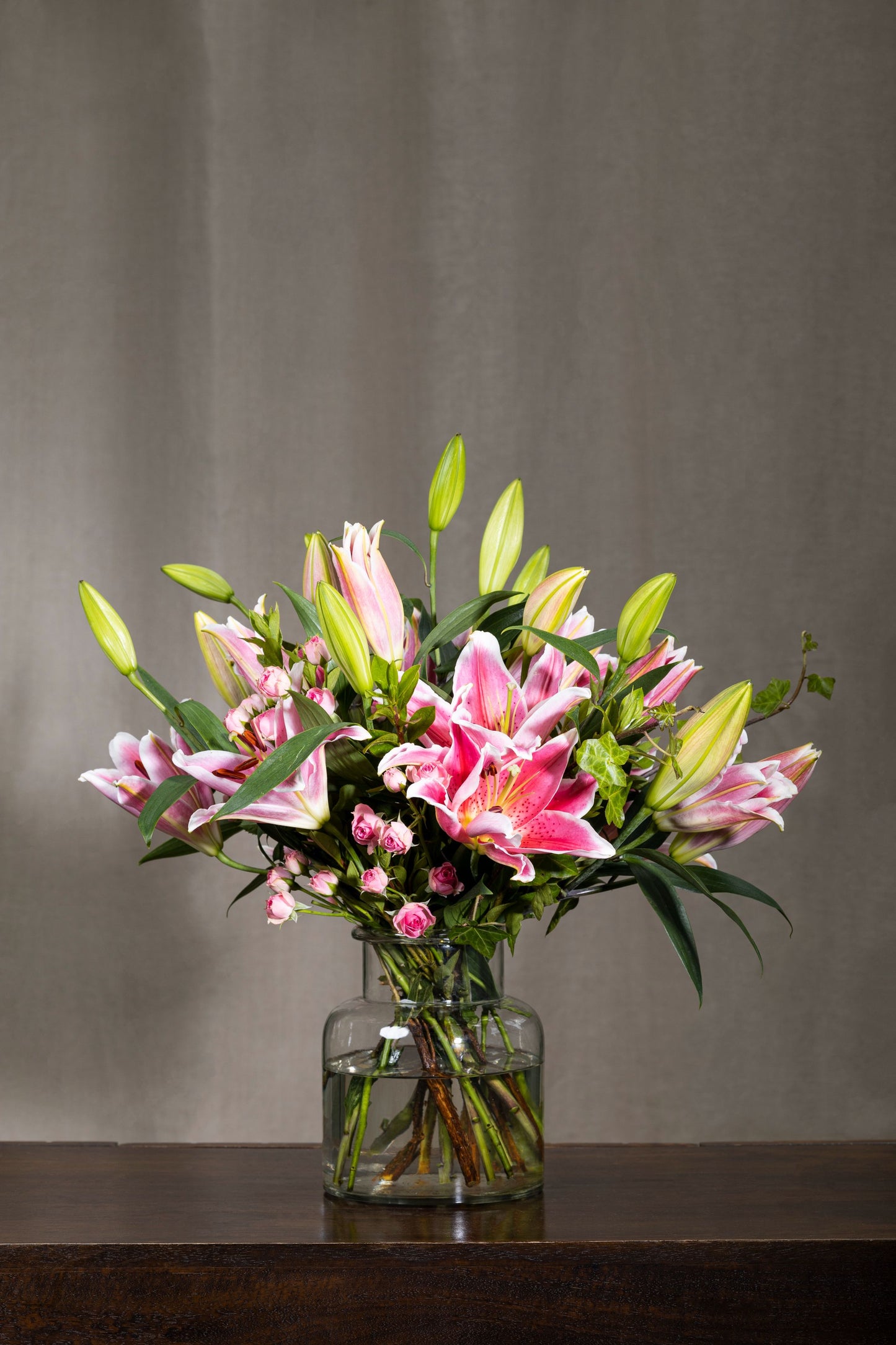 Charmer - Elegant Oriental Lilies and Spray Carnation flowers in a clear glass biscuit jar with lush foliage | Flower delivery in Bengaluru | Buy flower bouquets online Bengaluru | Same-day flower delivery Bengaluru | Online florist Bengaluru | Order flowers online Bengaluru | Luxury flower bouquet in Bengaluru