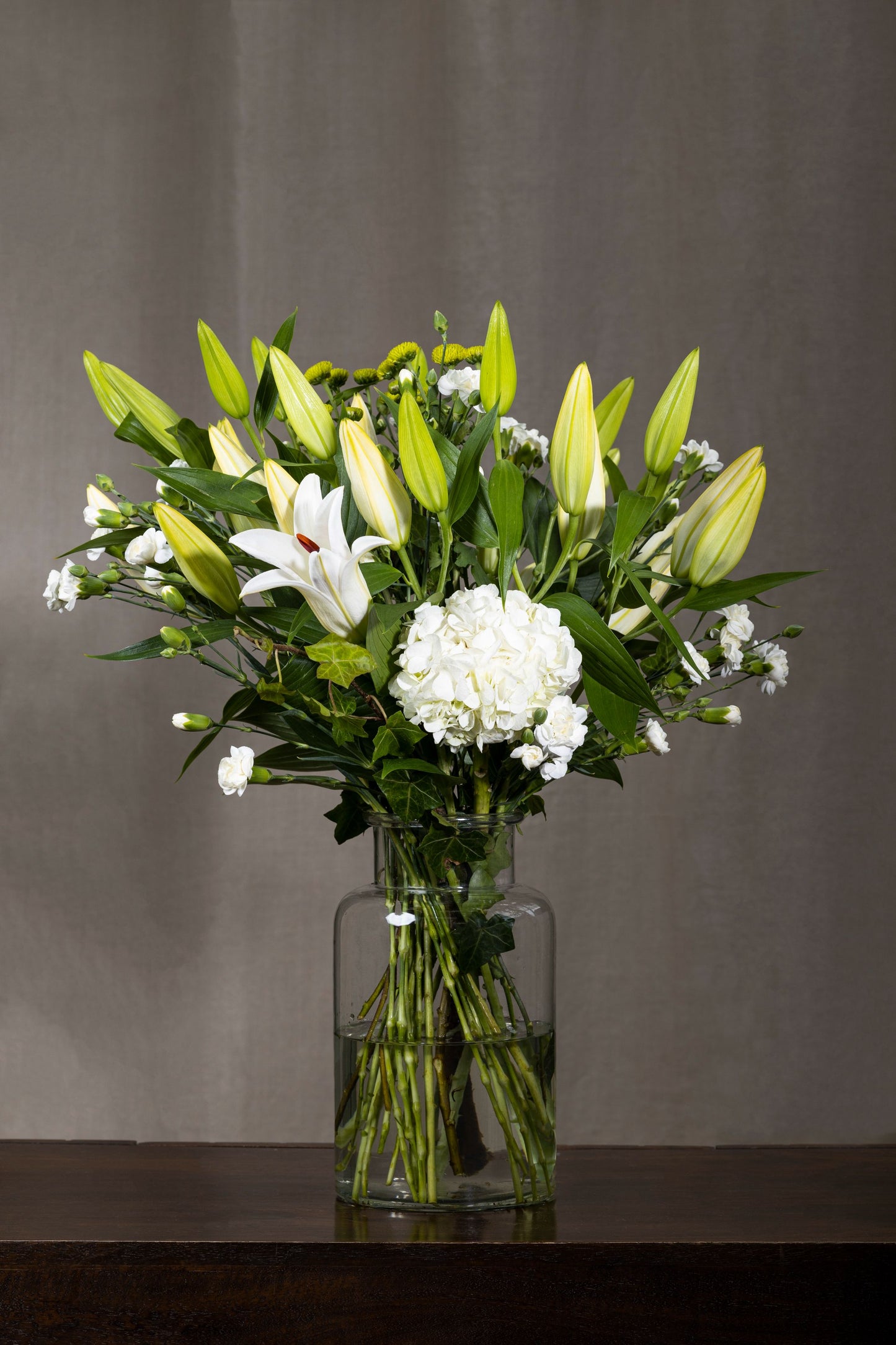 White Rhapsody - Elegant tall glass biscuit jar with pure white Oriental Lilies, misty Hydrangea bunches, and lush green foliage | Flower delivery in Bengaluru | Buy flower bouquets online Bengaluru | Same-day flower delivery Bengaluru | Online florist Bengaluru | Order flowers online Bengaluru | Luxury flower bouquet in Bengaluru