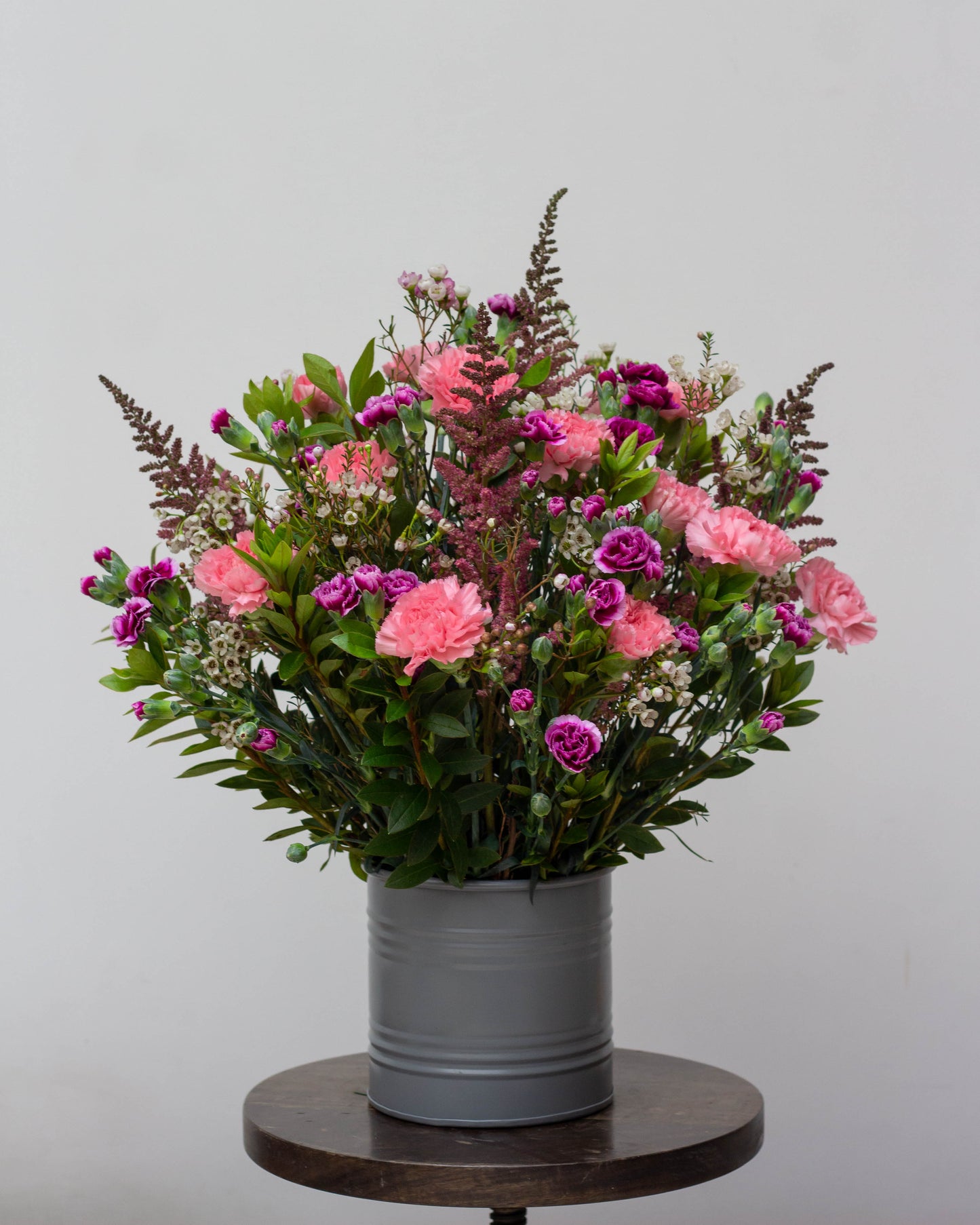 When I Fall in Love – A custom-painted round tin filled with Purple Spray Carnations, Pink Standard Carnations, Astilbe, and Wax Flowers, perfect for Valentine's Day, birthdays, anniversaries, congratulations, new baby celebrations, and thank you gifts. Flower delivery in Bengaluru | Buy flower bouquets online Bengaluru | Same-day flower delivery Bengaluru | Online florist Bengaluru | Order flowers online Bengaluru | Luxury flower bouquet in Bengaluru